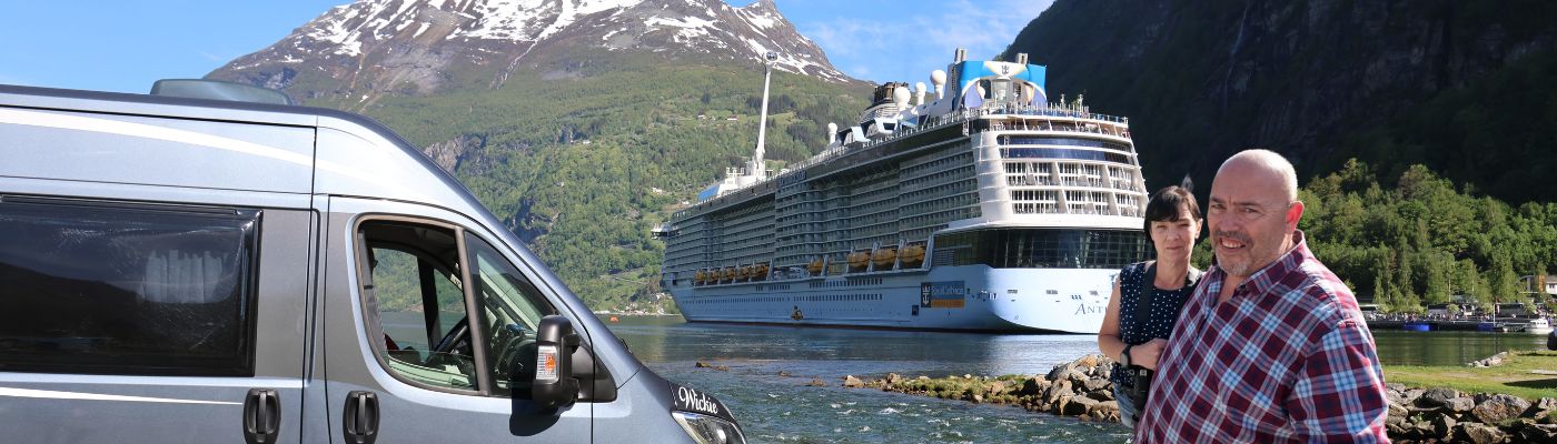 Robin und Kirsten mit ihrem Wohnmobil Wickie vor einem Kreuzfahrtschiff im Geirangerfjord, Norwegen