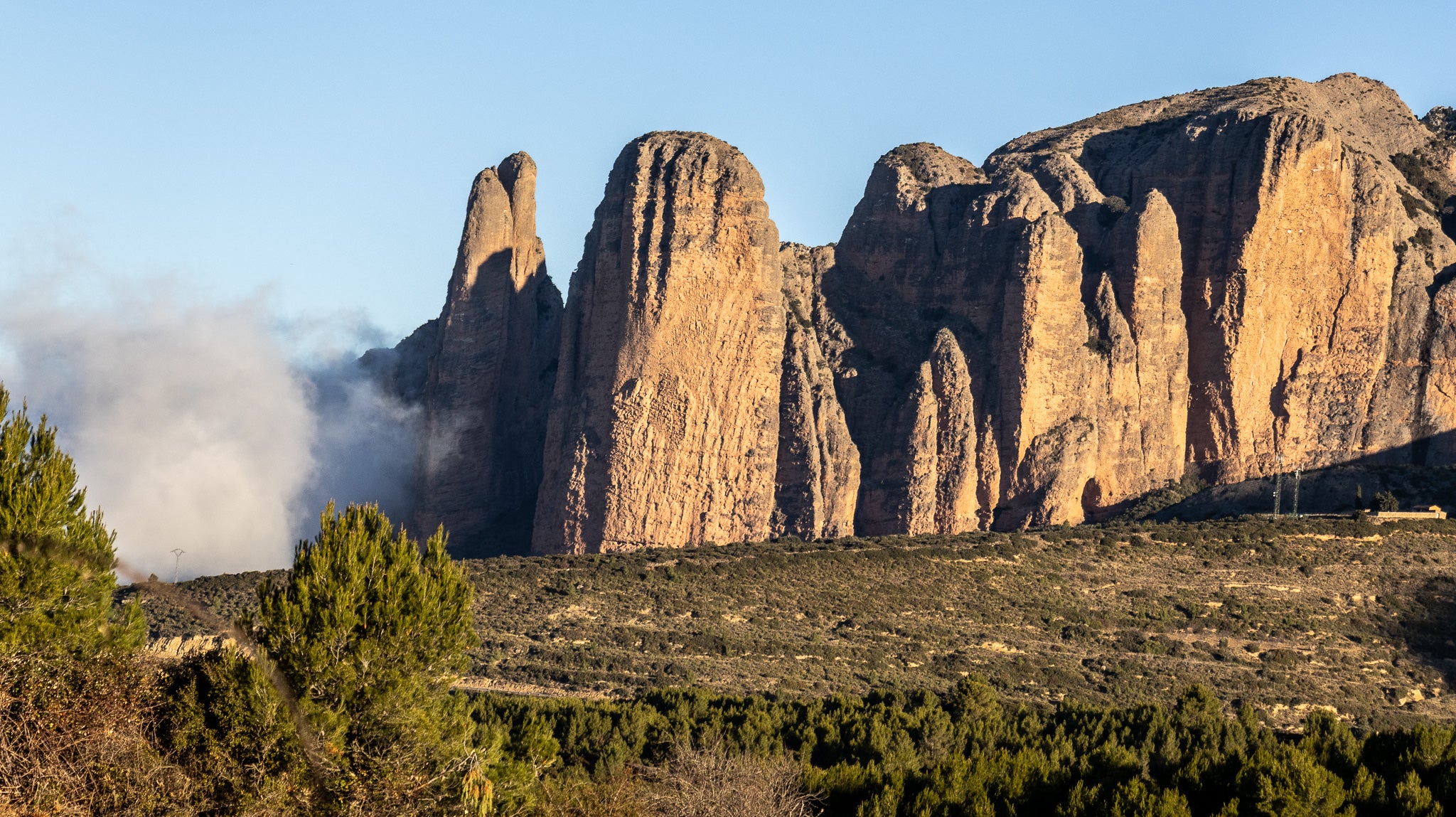 Die Mallos de Riglos im Morgenlicht in Aragonien, Spanien. Die gewaltigen roten Felsformationen zählen zu den bekanntesten Natursehenswürdigkeiten Nordspaniens und sind ein beliebtes Ziel für Kletterer und Wanderer.