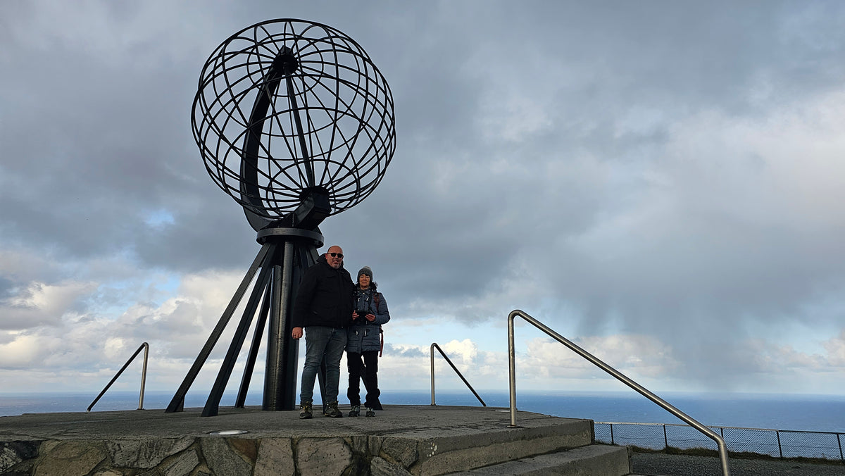 Zwei Reisende von Wickie On Tour stehen bei stürmischem Wetter vor dem berühmten Nordkapp-Globus in Norwegen.
